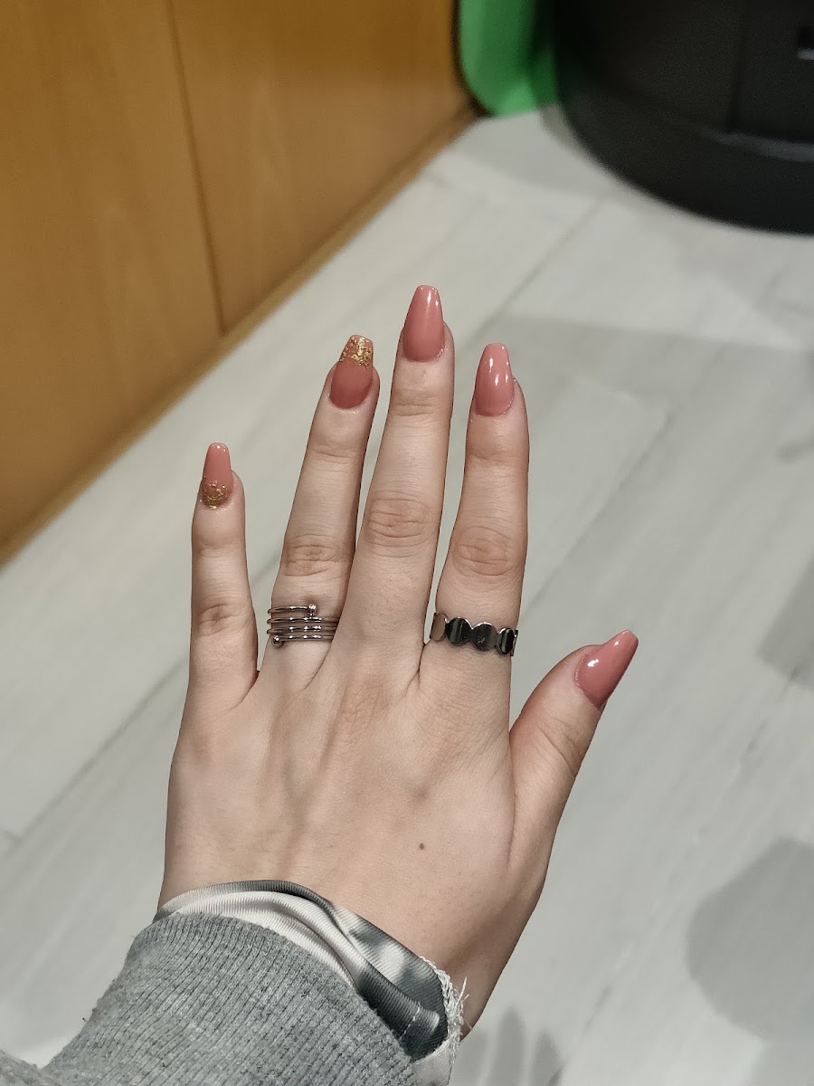 Manicura nude con glitter dorado en forma de media luna en las uñas del anular y meñique, con dos anillos