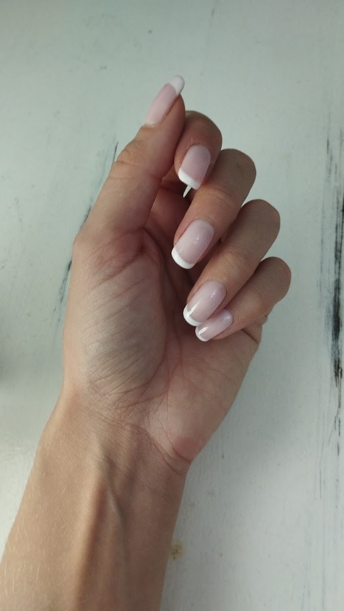 Mano con manicura francesa clásica en tonos rosados y blanco, sobre fondo claro