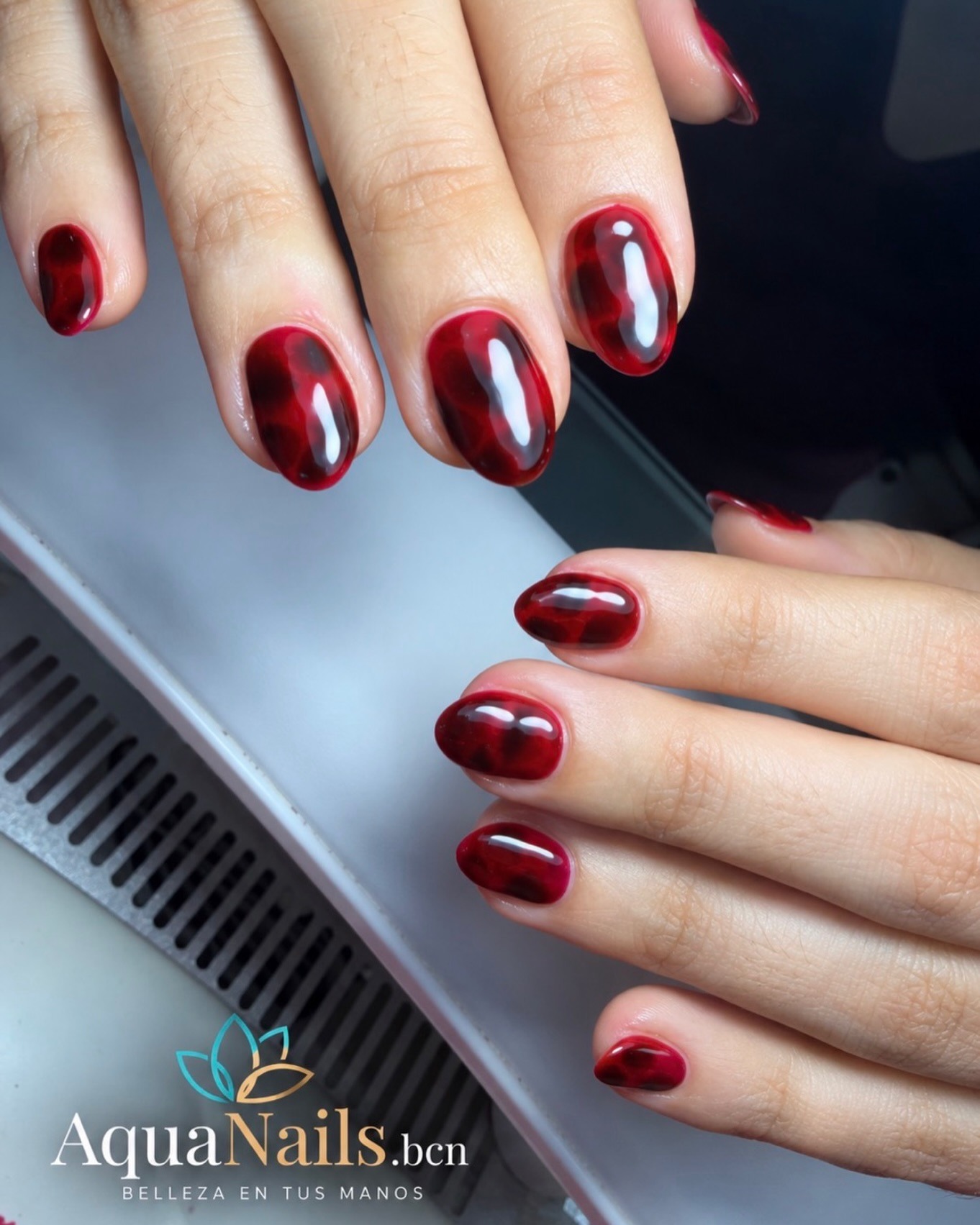 Manos con uñas ovaladas en tono rojo oscuro brillante